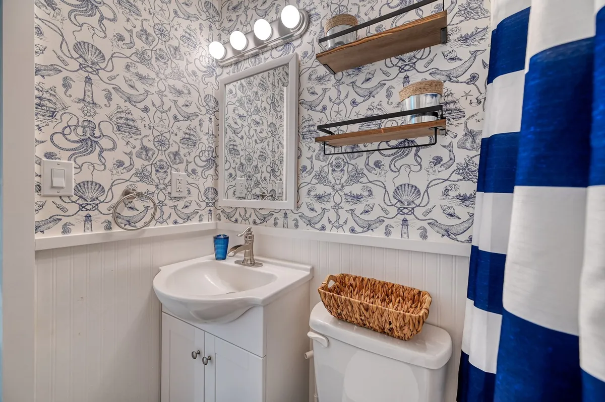 A bathroom with ornate wallpaper, a framed mirror, and a modern sink creates a cheerful setting for daily routines. The space feels fresh and relaxing—ideal for both quick morning prep and calming evening wind-downs.