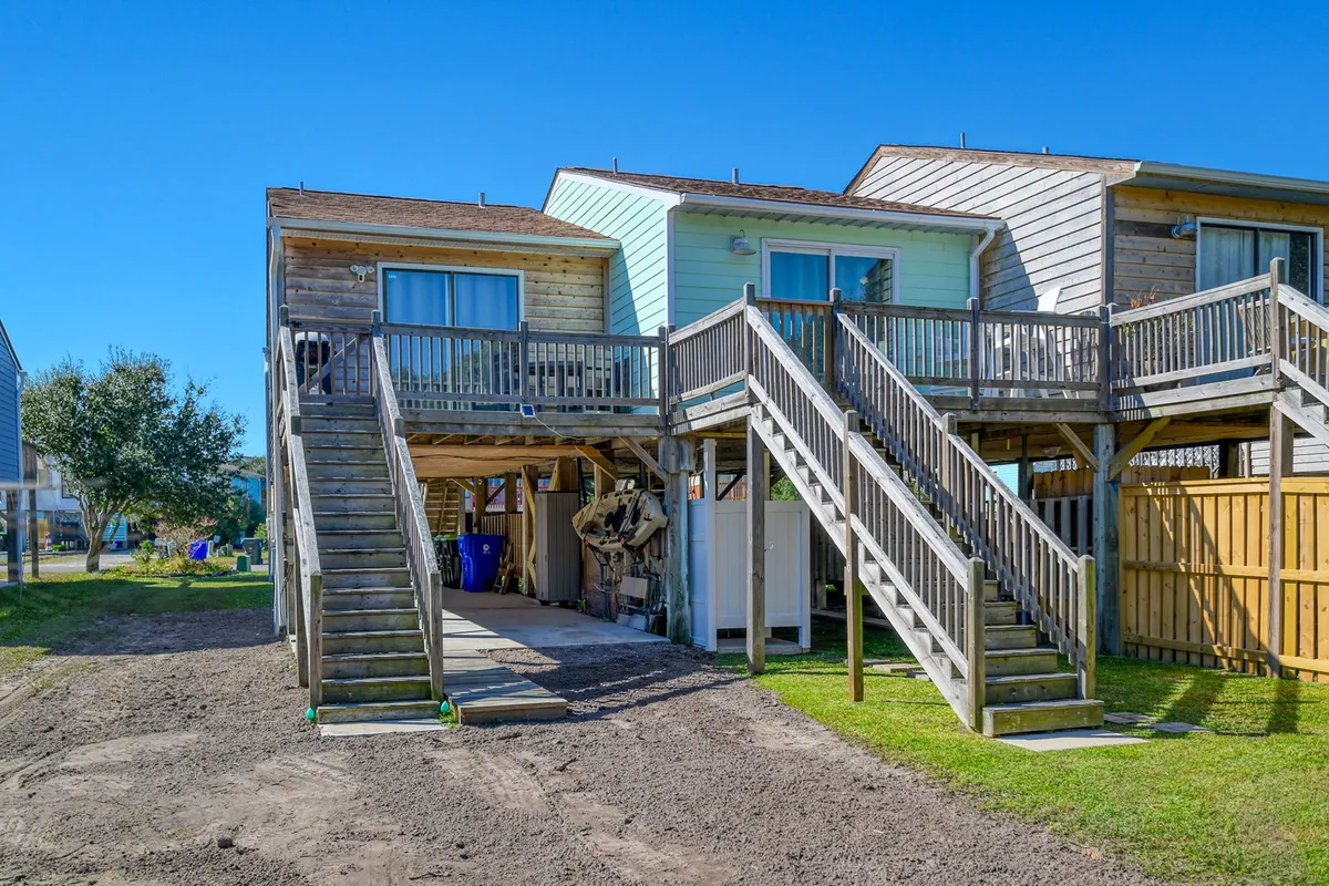 An exterior view showing dual wooden stairways leading up to separate decks, with both a green and a blue building visible. The deck area suggests opportunities for gatherings, enjoying sunset views, or morning coffee.