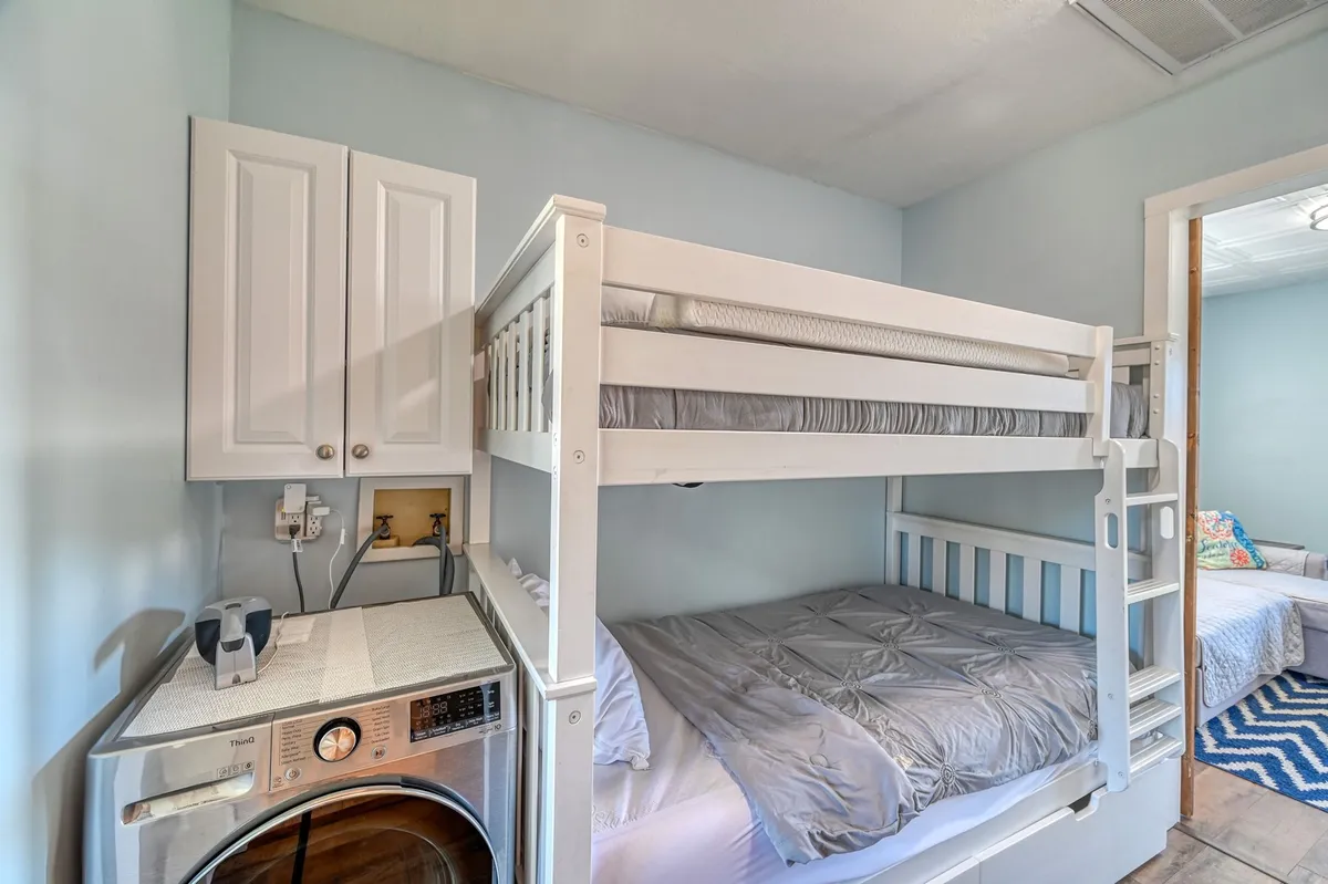 A compact interior scene showcases a cozy bunk bed setup next to a stackable washer/dryer unit. Light blue walls and practical furnishings create a functional area ideal for family stays and efficient laundry sessions.