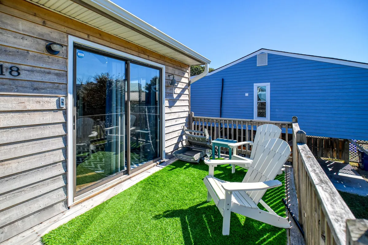 This image captures a wooden deck outfitted with Adirondack chairs and a glass door leading inside, set up for moments of relaxation, reading, or social gatherings. The outdoor setting is casual, offering a direct connection to nature and a private space for lounging with a pet.