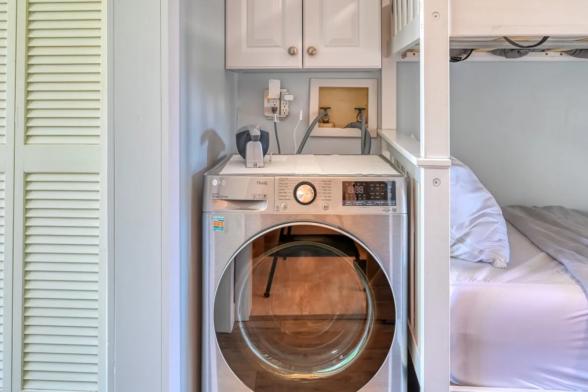A practical interior corner featuring a washing machine beneath cabinets and a cozy bunk bed nearby. The space highlights both convenience for quick chores like laundry and the comfort of a restful sleeping area, emphasizing a no-fuss, flexible stay.