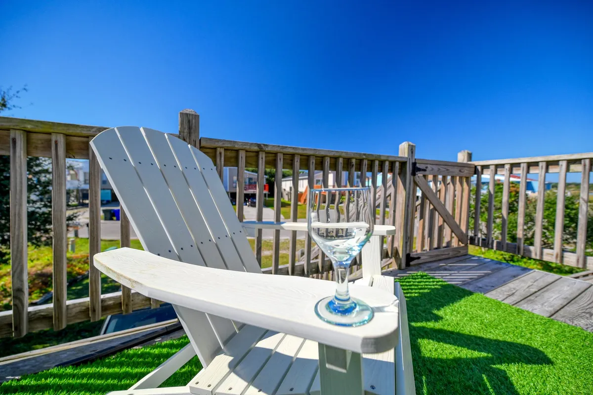 A tranquil outdoor setup with an Adirondack chair and a martini glass resting on the wooden railing, overlooking a peaceful, natural setting. The image evokes a sense of relaxation and unwinding after a day at the beach, hinting at sunset views and leisurely downtime on the deck.